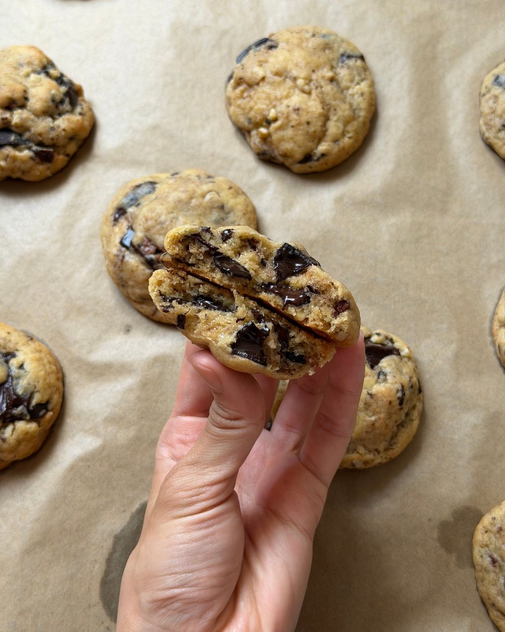 Una mano sujeta una cookie partida por la mitad, con el chocolate derretido, sobre papel de horno